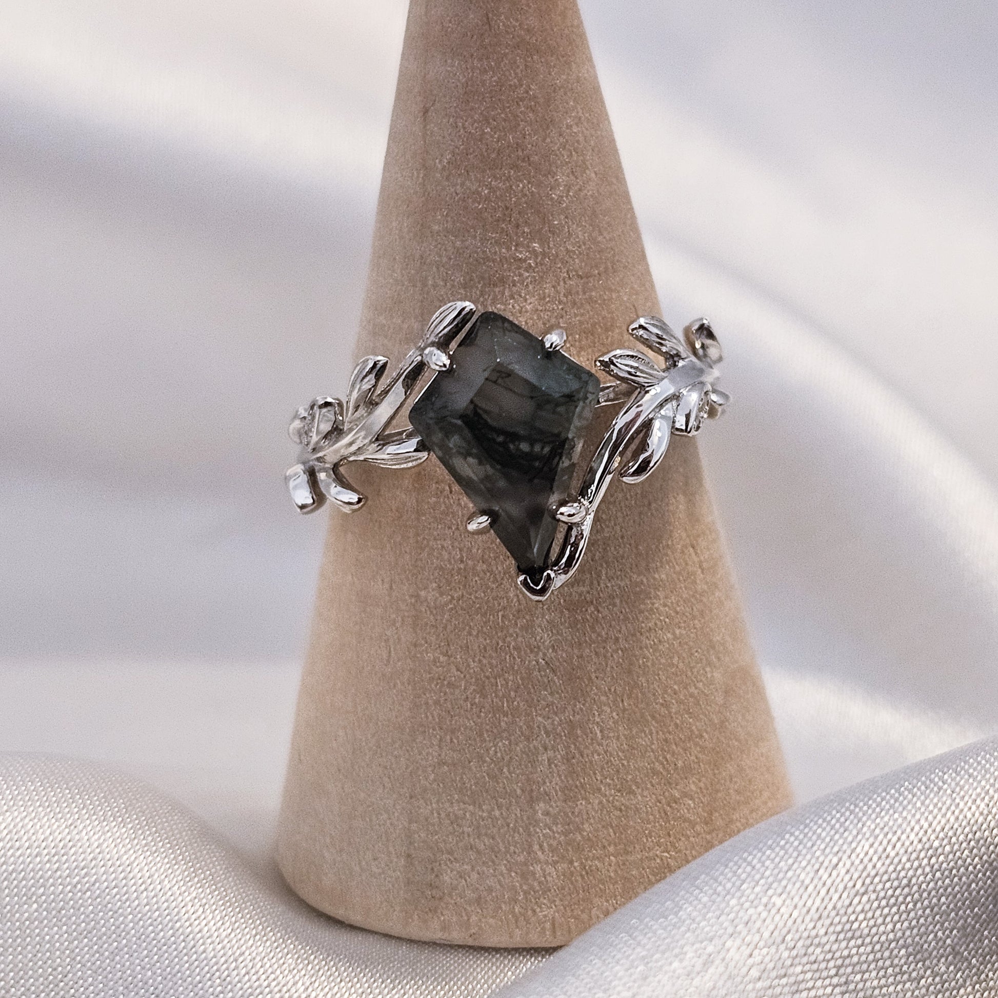 moss agate ring with leaf design on a ring holder with silk background