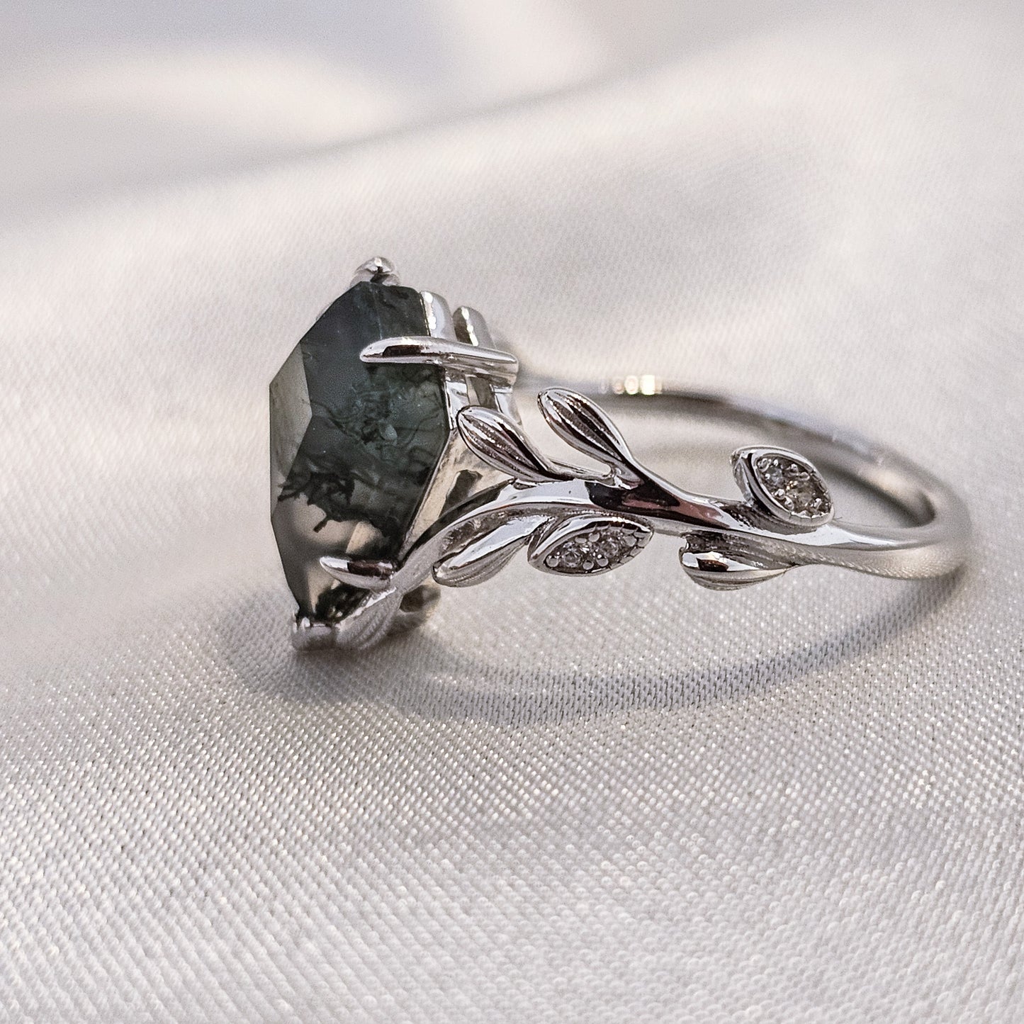 side view of a moss agate kite cut ring with leaf detail on a silk background