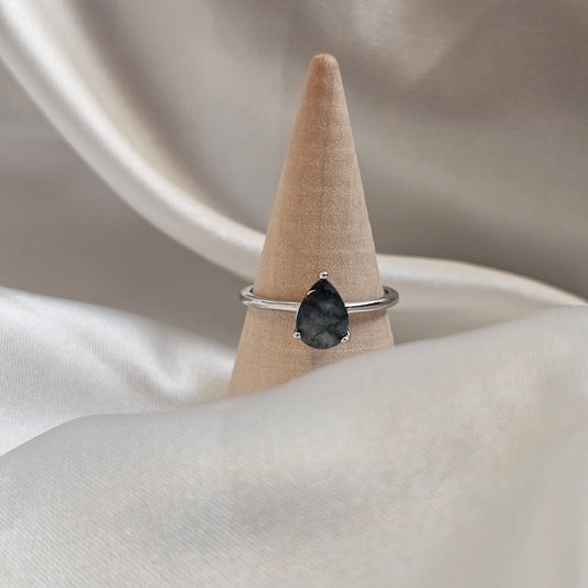 Silver ring with a black gemstone on a beige stand against a neutral background