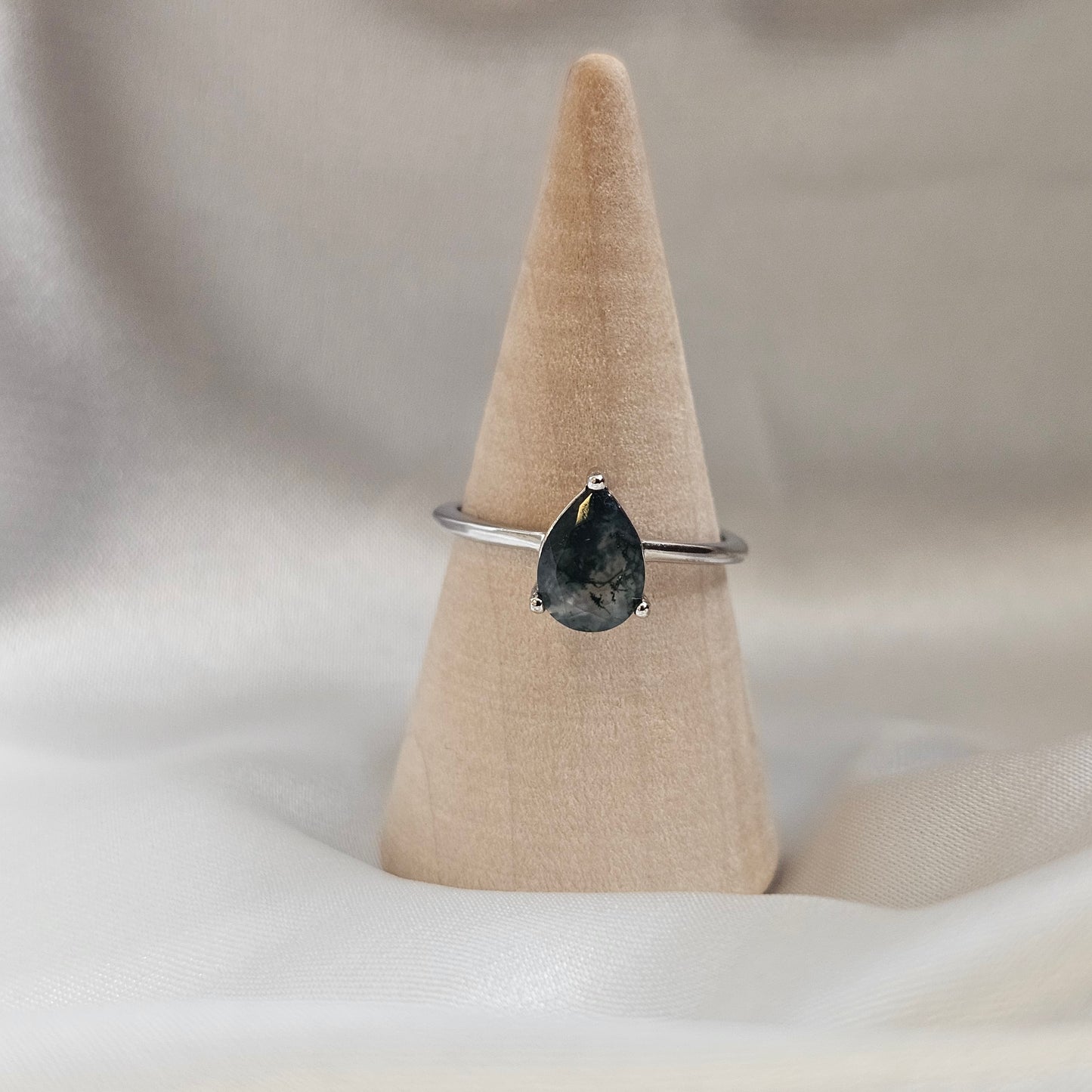 Silver bracelet with a black teardrop-shaped gemstone on a beige cone against a white background