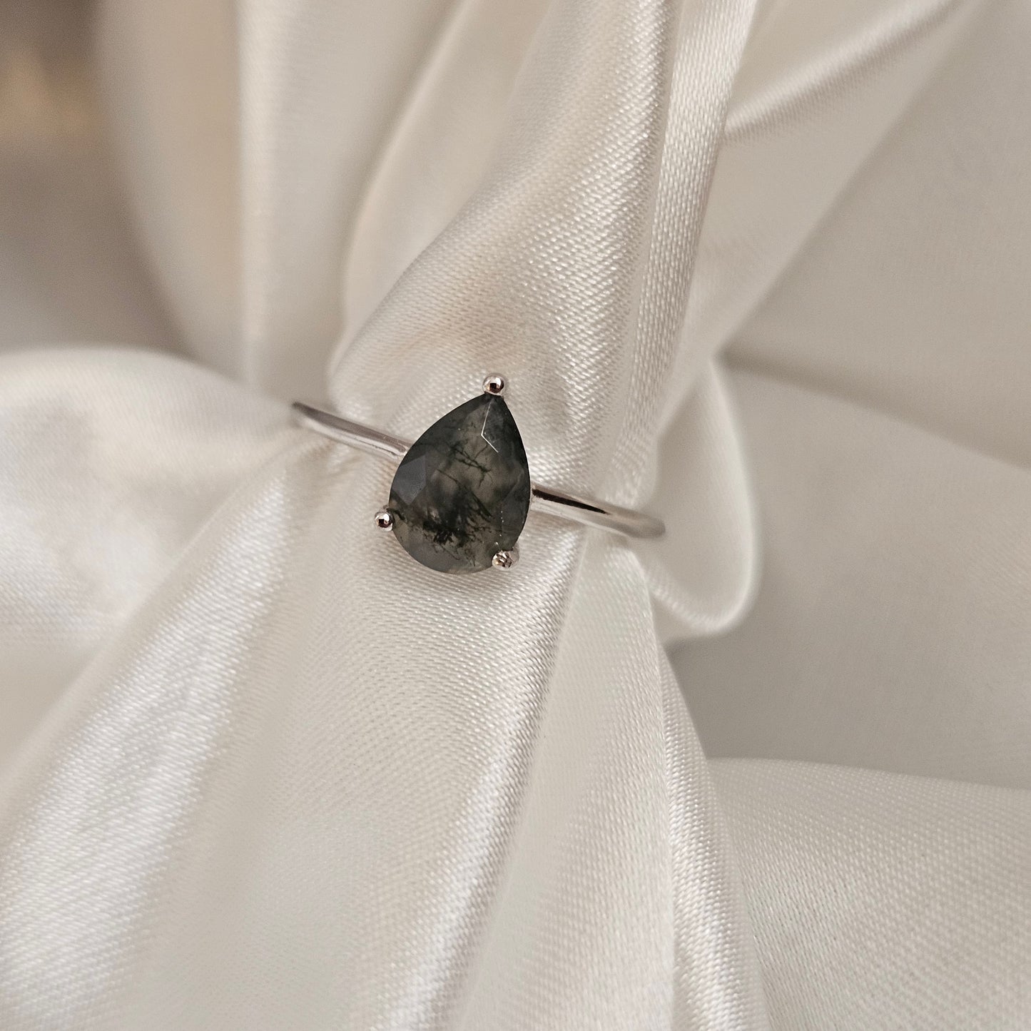 Silver ring with a dark gemstone on a white fabric background