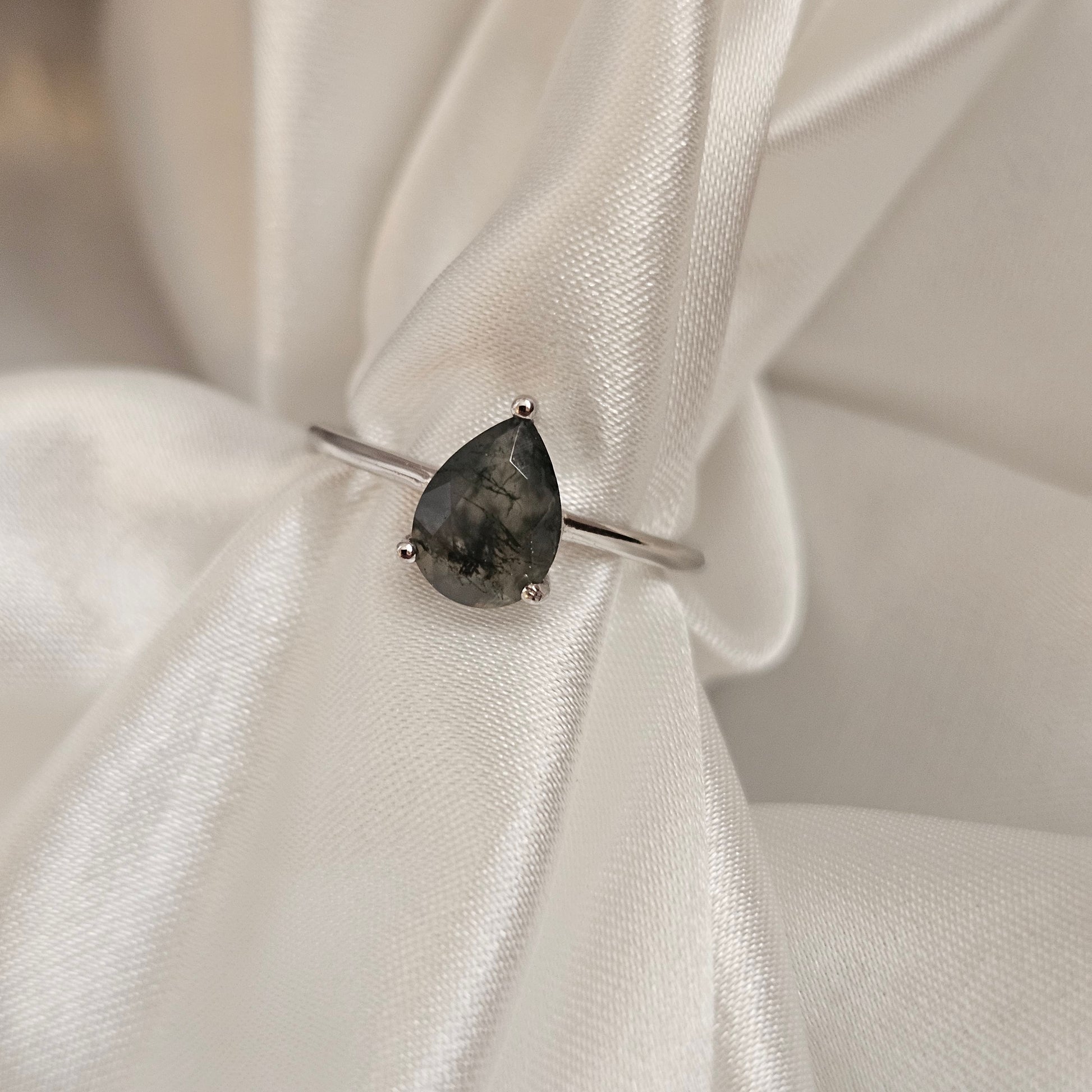 Silver ring with a dark gemstone on a white fabric background