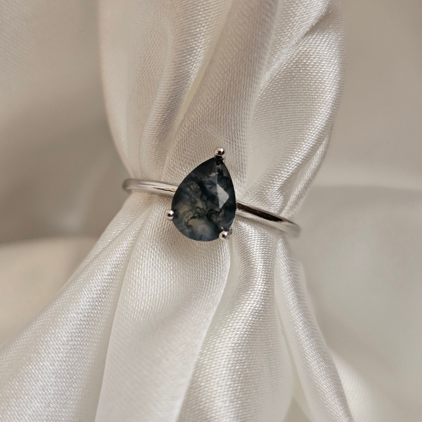 Silver ring with a dark gemstone on a white fabric background