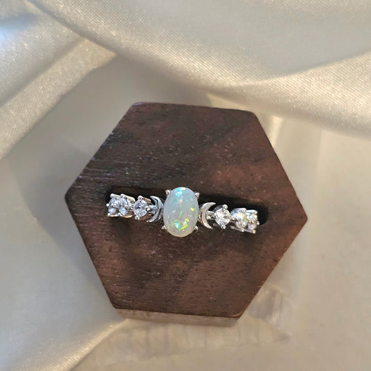 white opal  ring with a central gemstone on a wooden stand