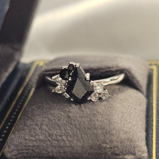 Silver ring with black gemstone and smaller diamonds on a textured surface