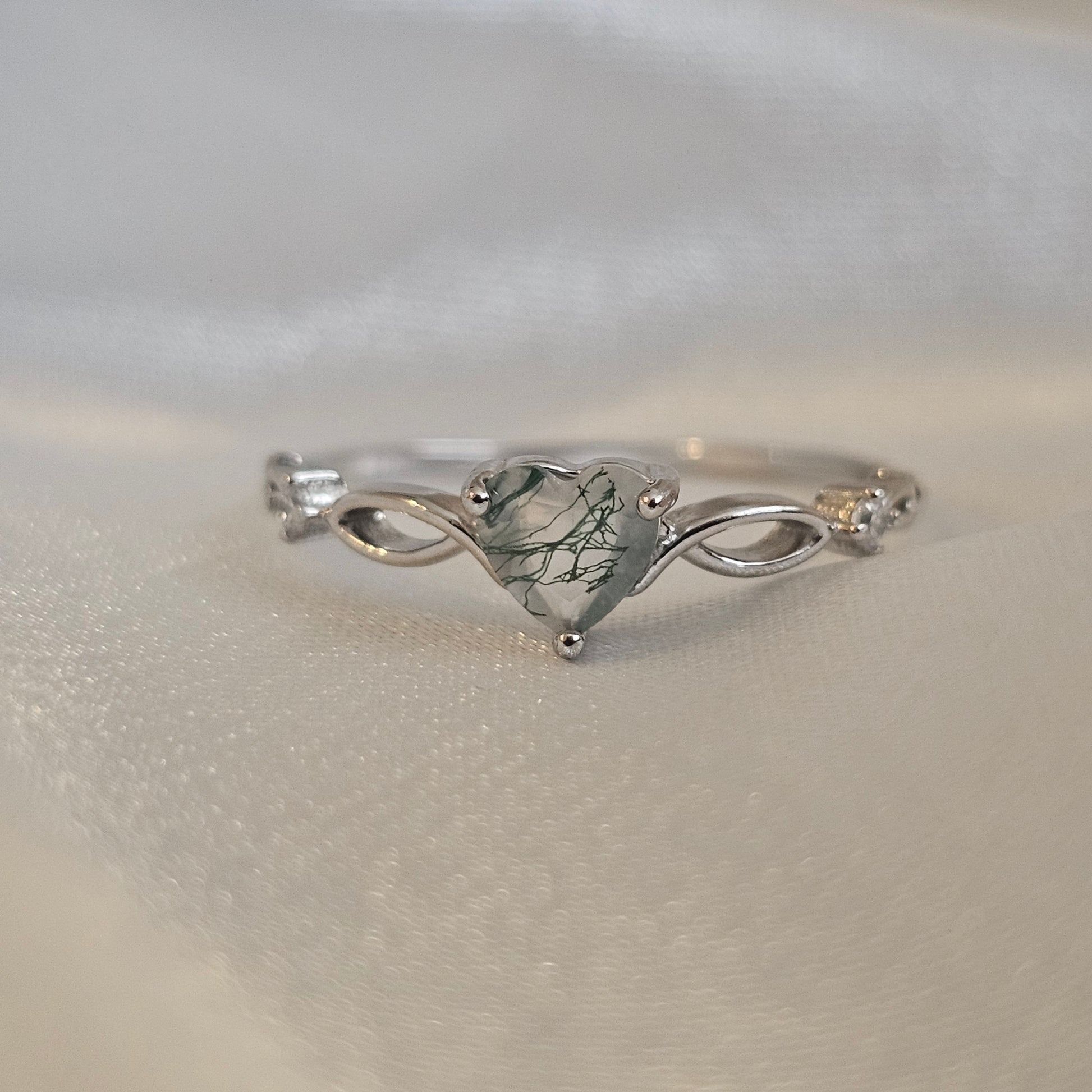 Natural Moss Agate heart-cut gemstone ring in sterling silver with infinity design — Evergreen Heart Ring on satin background.