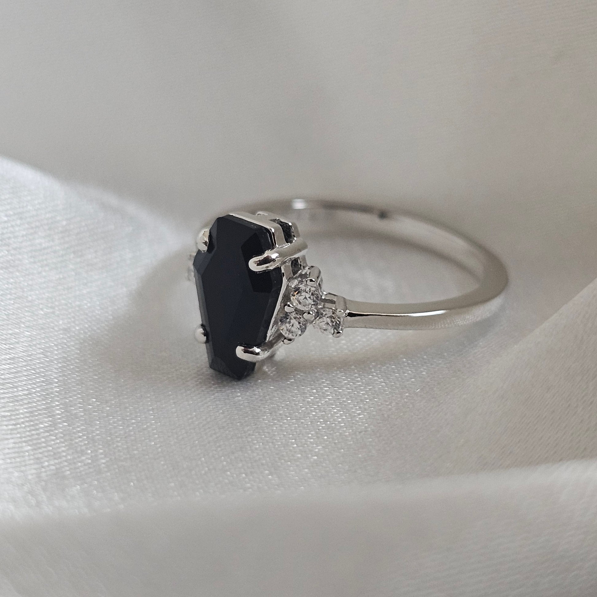Silver ring with a black onyx gemstone and small diamonds on a white fabric background