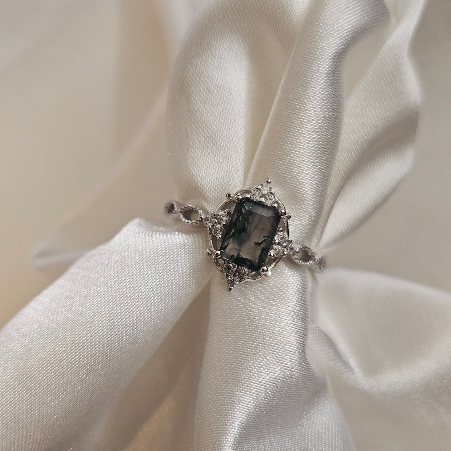 Silver pendant with a dark gemstone  moss agate on white satin fabric