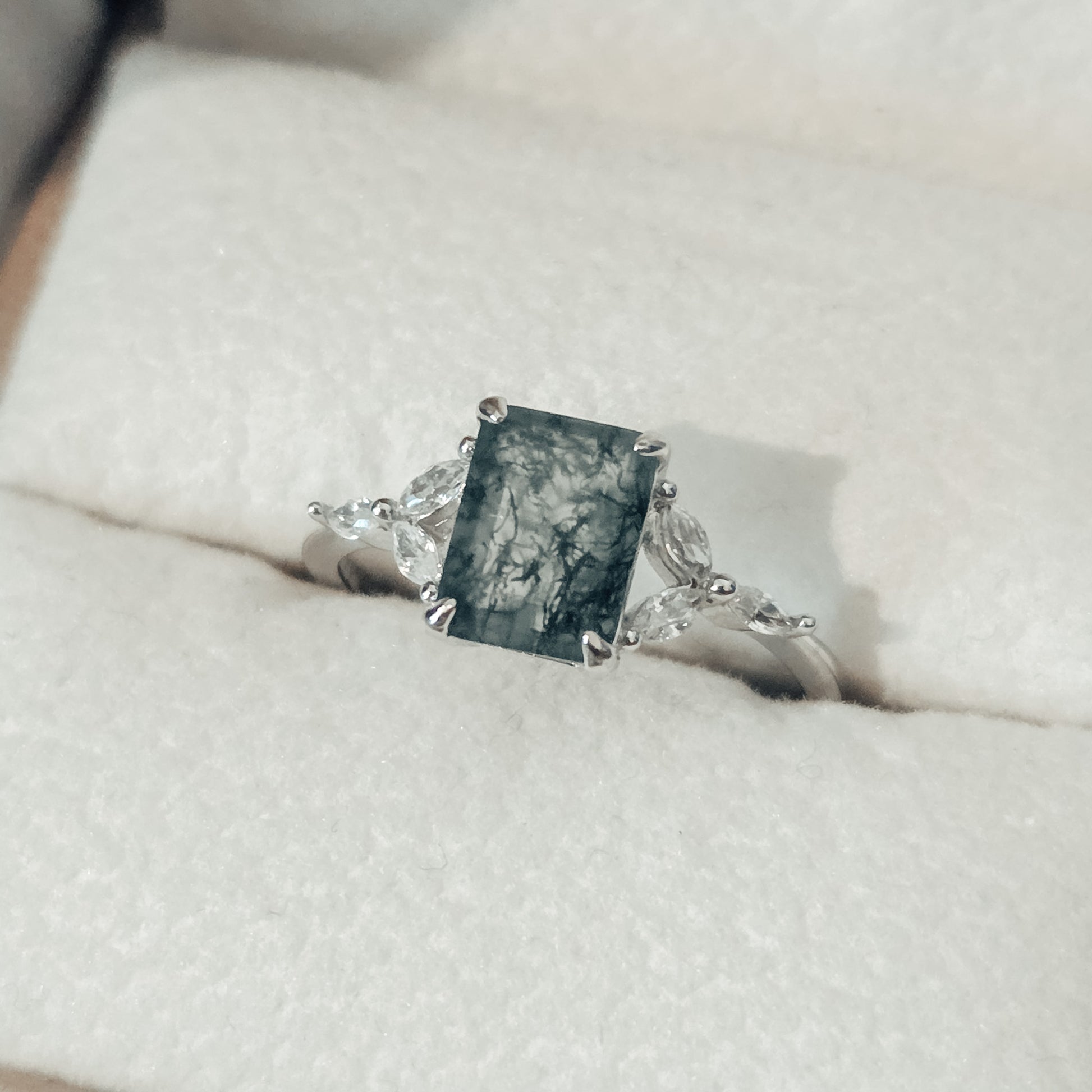 Close-up of a natural moss agate ring featuring a square-cut moss agate centre stone with distinctive dark green moss-like inclusions, set in solid 925 sterling silver. The moss agate gemstone is framed by delicate white cubic zirconia accents on either side, highlighting the organic patterns within the stone. This nature-inspired moss agate ring showcases a unique one-of-a-kind gemstone, part of the Whispers of the Forest collection by Moonstone & Sage.