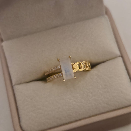 Gold ring with a rectangular moonstone main stone with cubic zirconia accent stones 925 silver 14k gold plating on a beige cushion