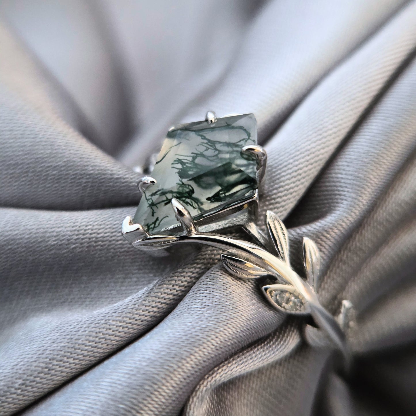 Olive Grove natural moss agate ring set in 925 sterling silver with platinum plating, showing a square-cut moss agate stone with leaf-inspired band on soft grey fabric