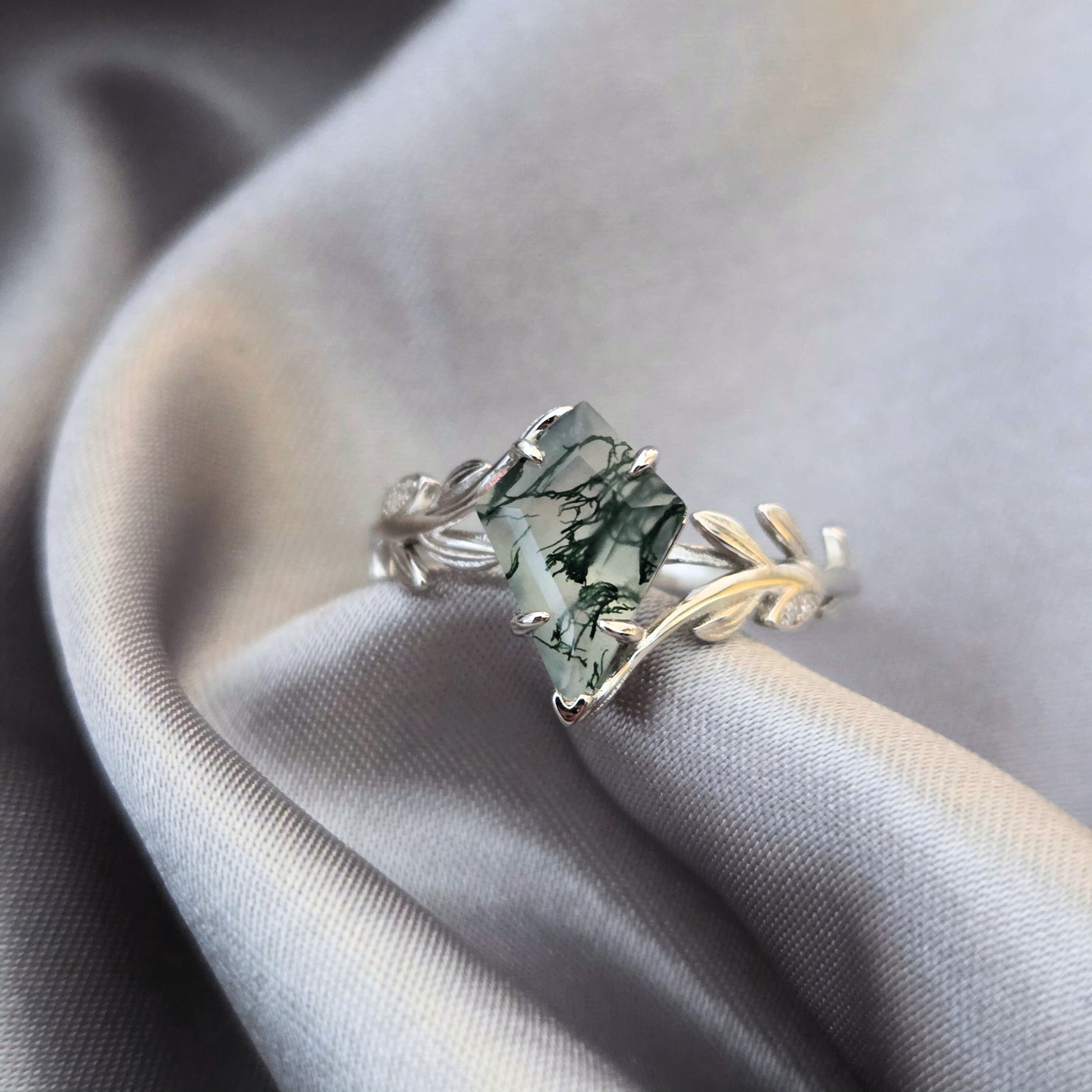 Olive Grove natural moss agate ring in 925 sterling silver with platinum plating, featuring a square-cut moss agate stone and leaf-inspired band on soft flowing fabric