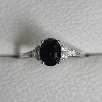 Silver ring with a dark gemstone on a light gray background