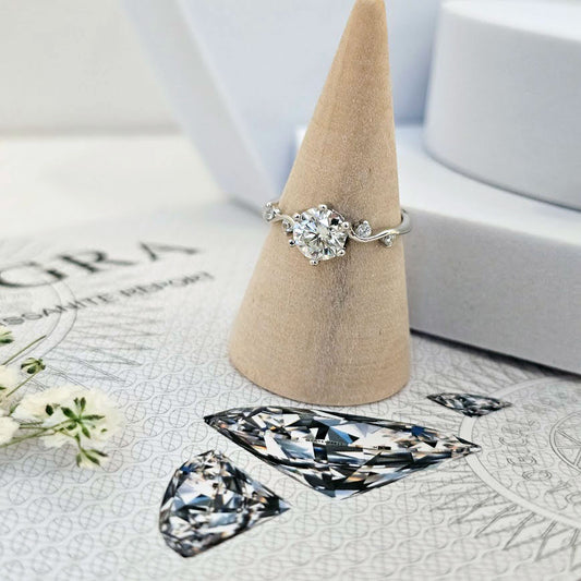 Moissanite engagement ring with twisting vine band and round brilliant-cut center stone displayed on beige cone stand on GRA certificate paper with diamond illustrations