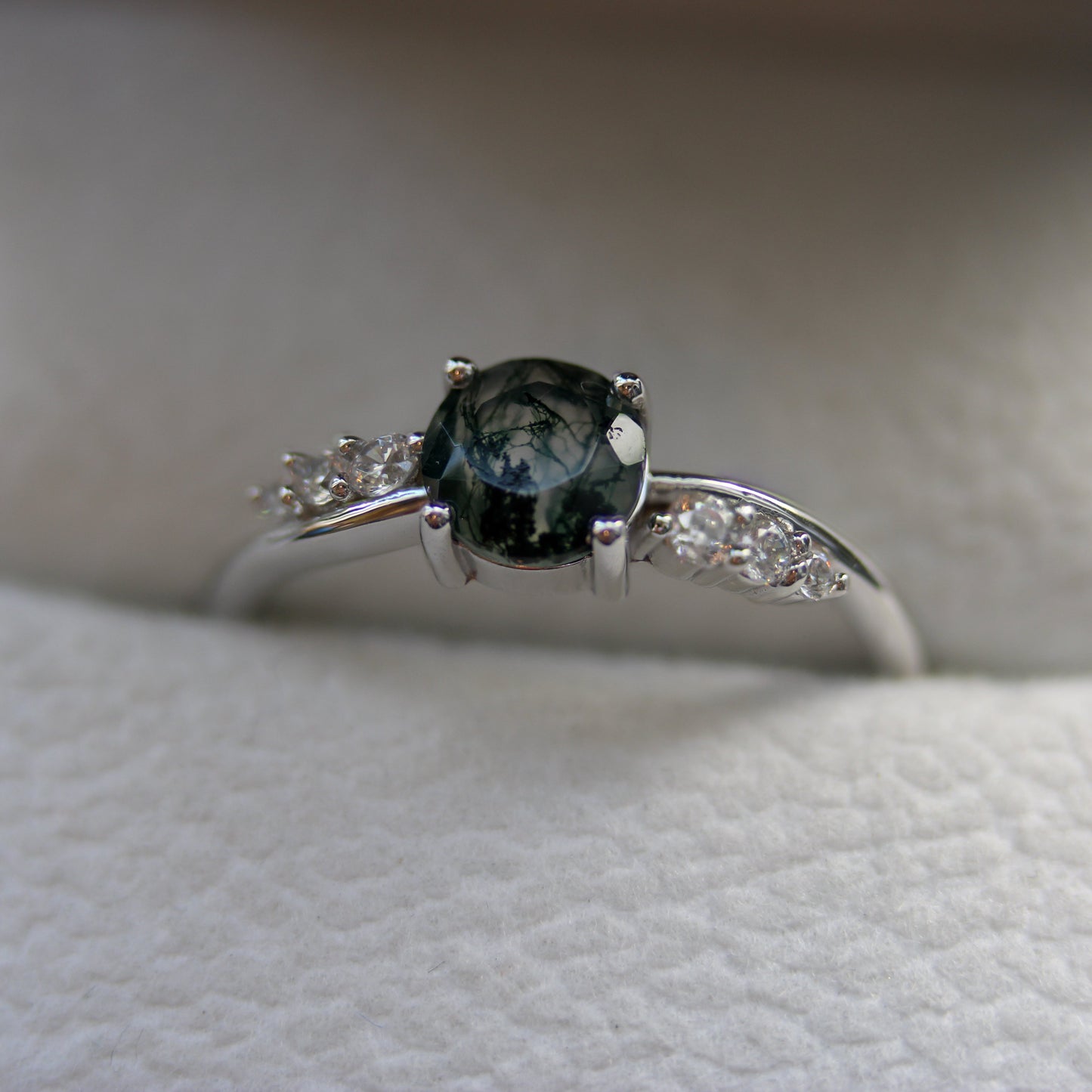 Close-up of a natural moss agate ring featuring an oval moss agate gemstone and sparkling cubic zirconia accent stones, set in 925 sterling silver and displayed in a jewellery box.