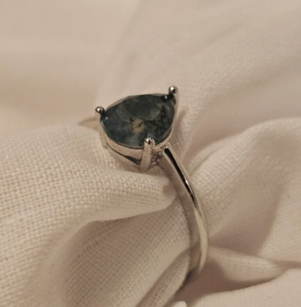 Silver ring with a green gemstone on a beige fabric background