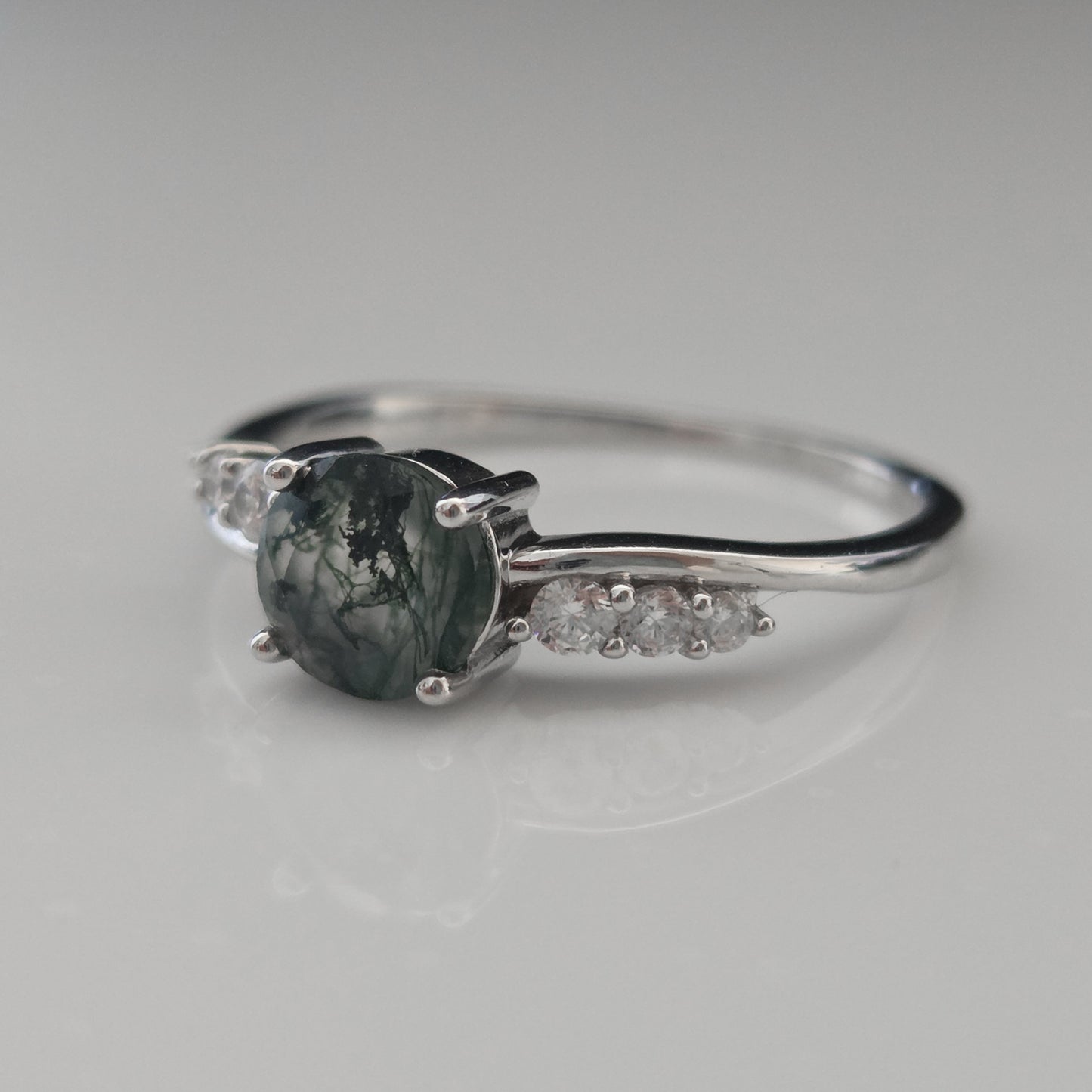 Side view of a natural moss agate ring featuring an round moss agate gemstone with cubic zirconia accent stones, crafted in 925 sterling silver and photographed against a soft white background.