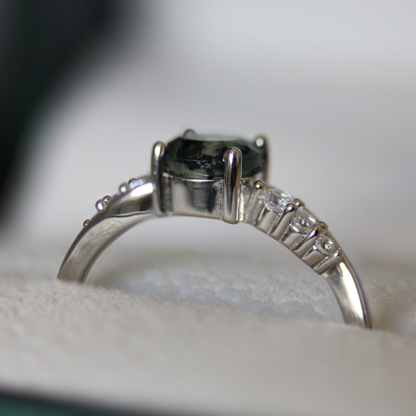 Side profile of a natural moss agate ring featuring a round moss agate gemstone and cubic zirconia accent stones, set in 925 sterling silver and displayed in a jewellery box.