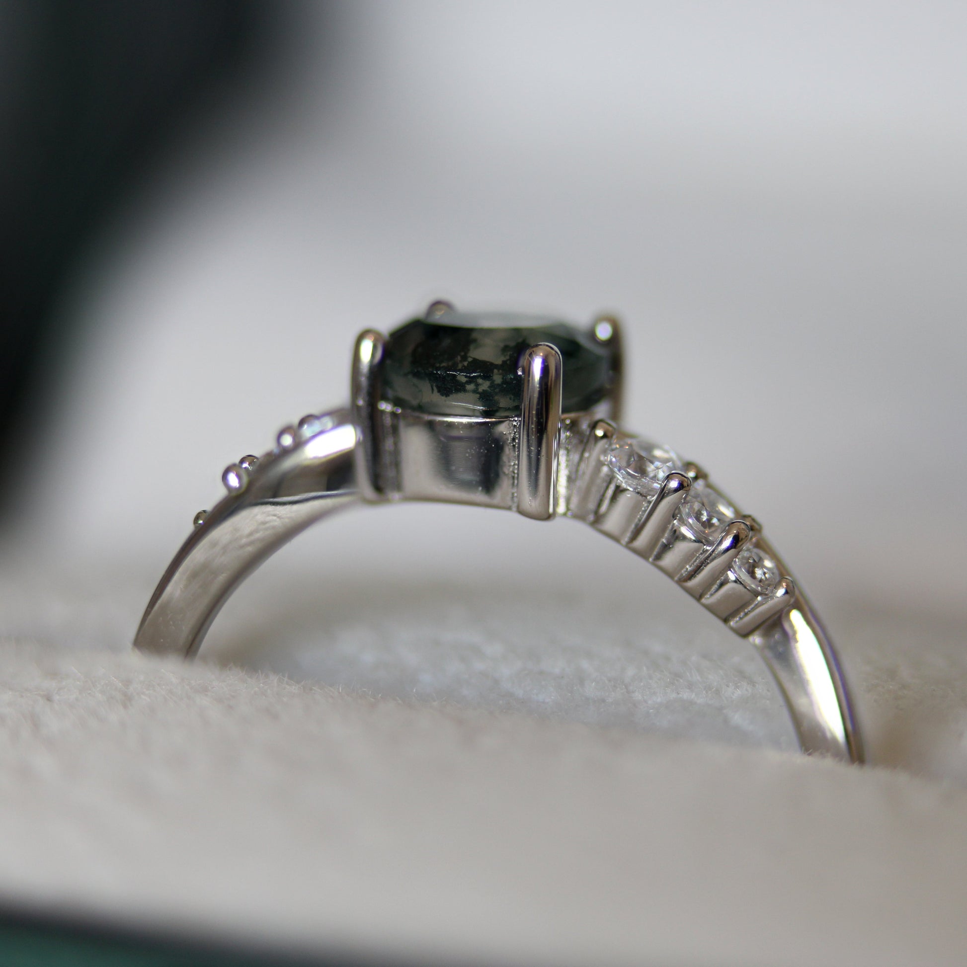 Side profile of a natural moss agate ring featuring a round moss agate gemstone and cubic zirconia accent stones, set in 925 sterling silver and displayed in a jewellery box.