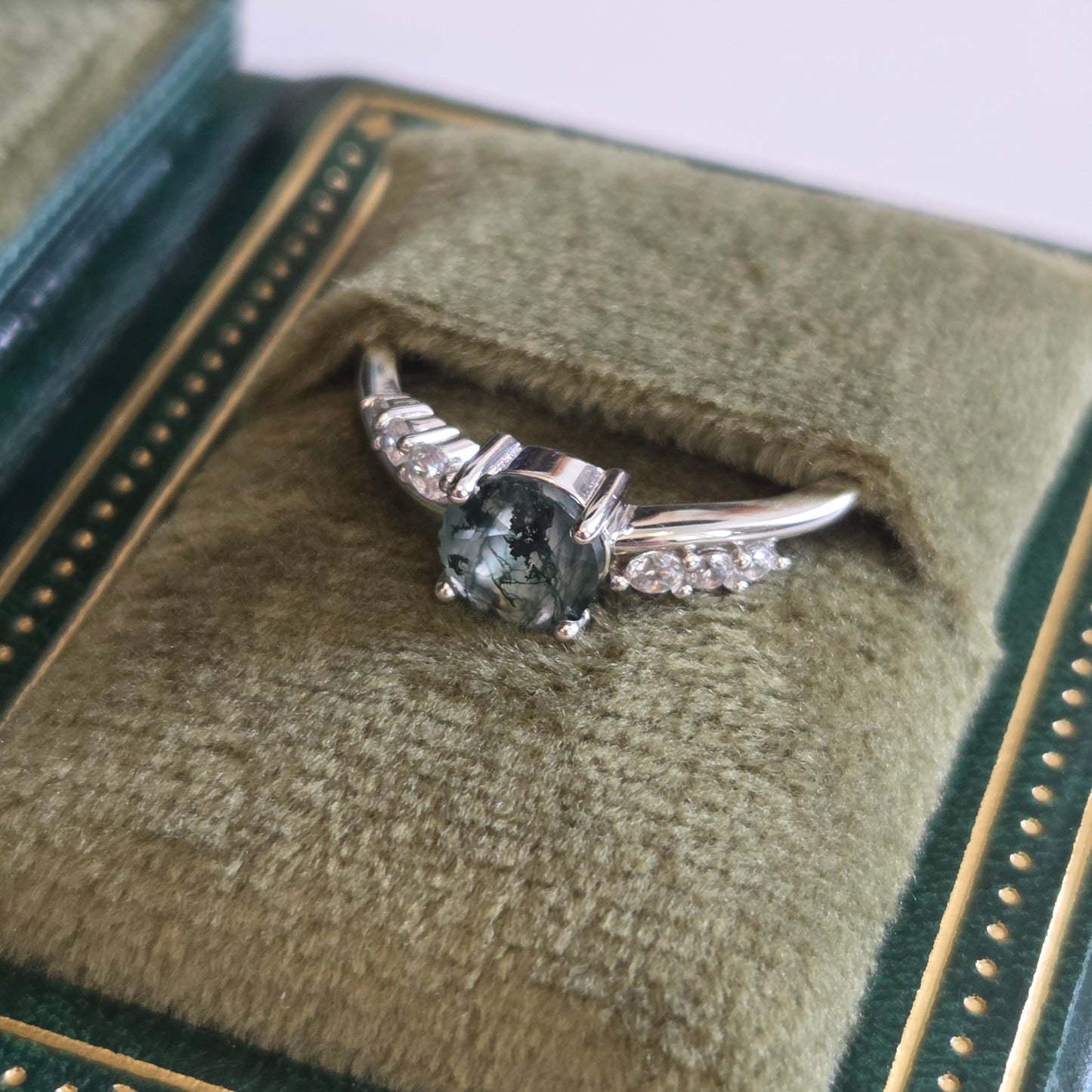 Natural moss agate ring with an oval moss agate gemstone and sparkling cubic zirconia accents, displayed in a green book-style jewellery box. Crafted in 925 sterling silver and inspired by nature.