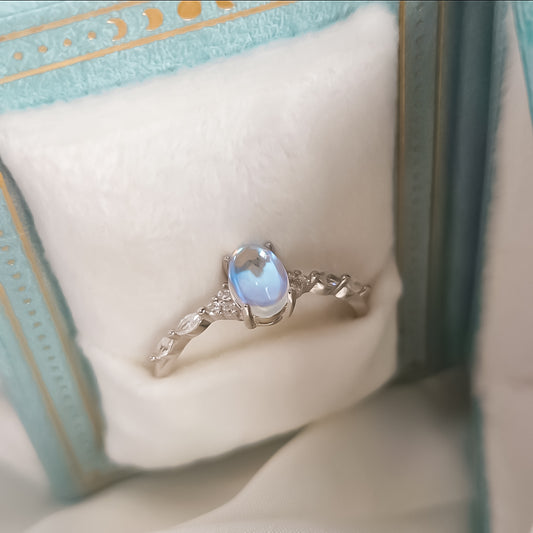Lab-created moonstone ring set in 925 sterling silver with delicate leaf-style band, displayed in a celestial light blue book-style ring box with gold detailing and soft faux fur lining.