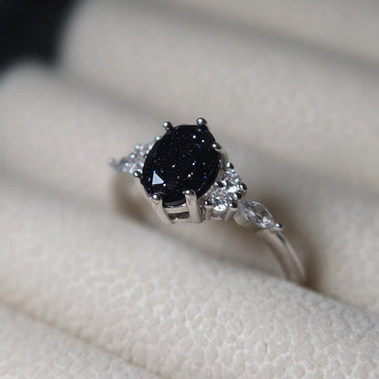 Silver ring with a dark sparkly gemstone on a neutral background