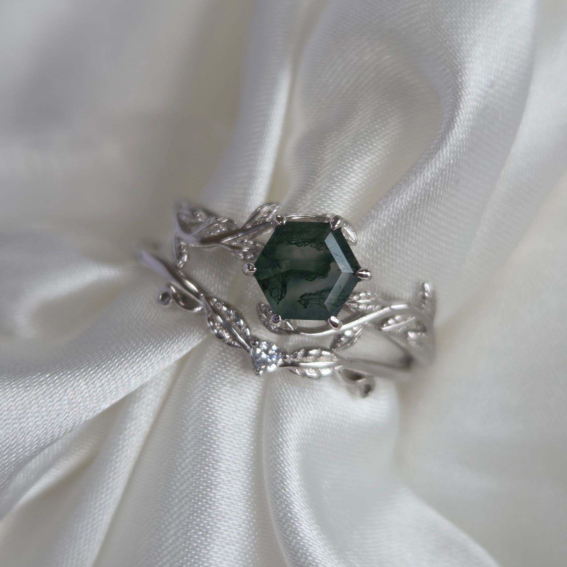 Moss agate bridal set with natural green moss agate stone and sterling silver engagement ring and wedding band with cubic zirconia accents on white satin fabric, nature-inspired wedding jewellery.