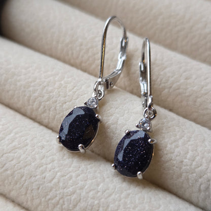 Pair of silver earrings with dark gemstones on a beige fabric background