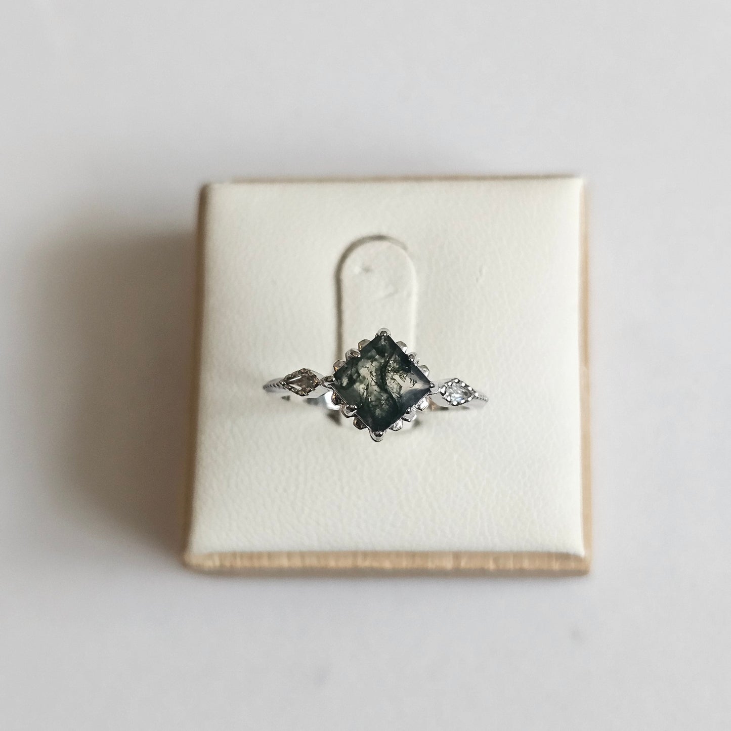 Silver ring with a solitaire Moss Agate Stone on a white box against a light gray background