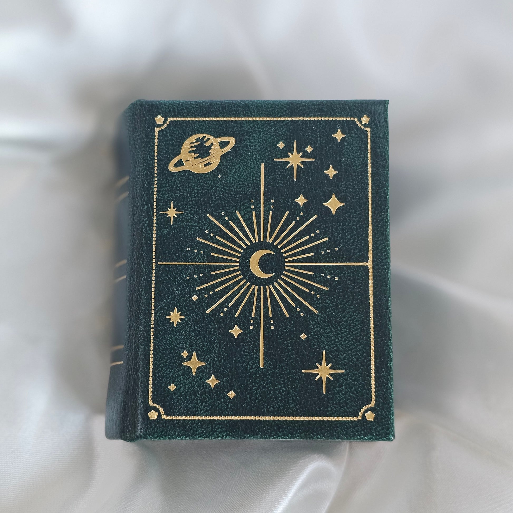 Dark green book with gold celestial designs on a white fabric background