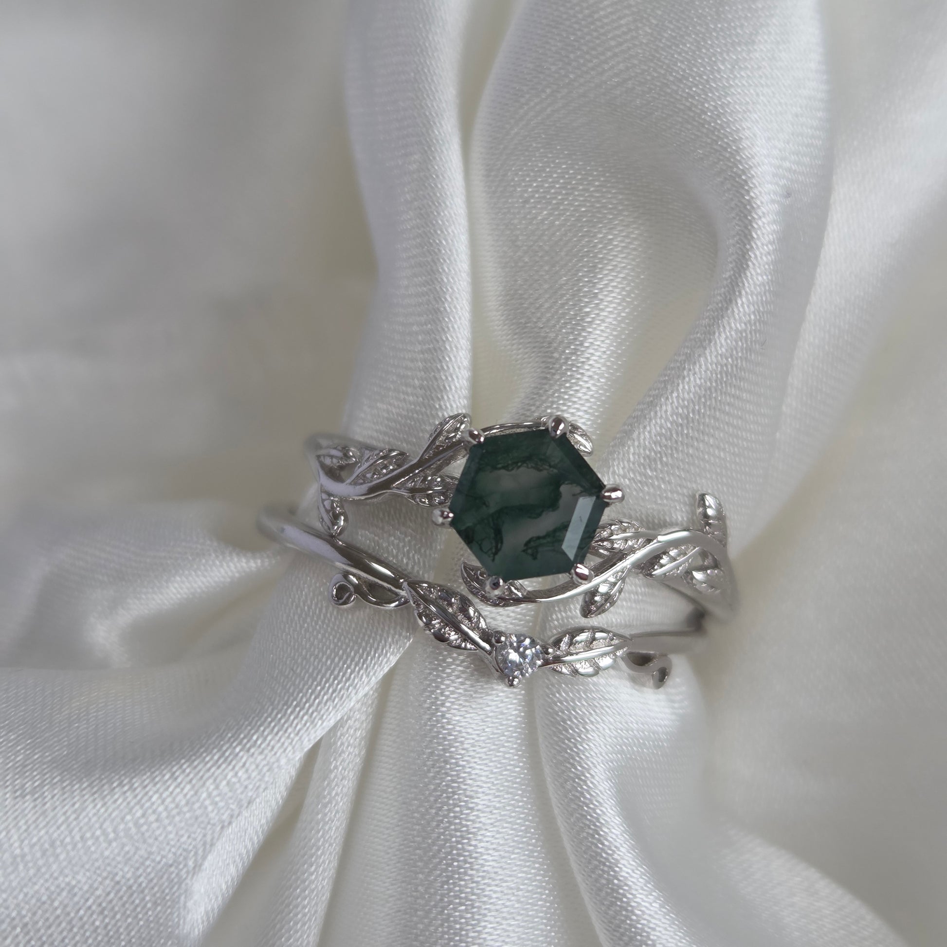 Moss agate bridal set with green moss agate stone and sterling silver engagement ring resting on white fabric, accented with sparkling cubic zirconia in a nature-inspired design.