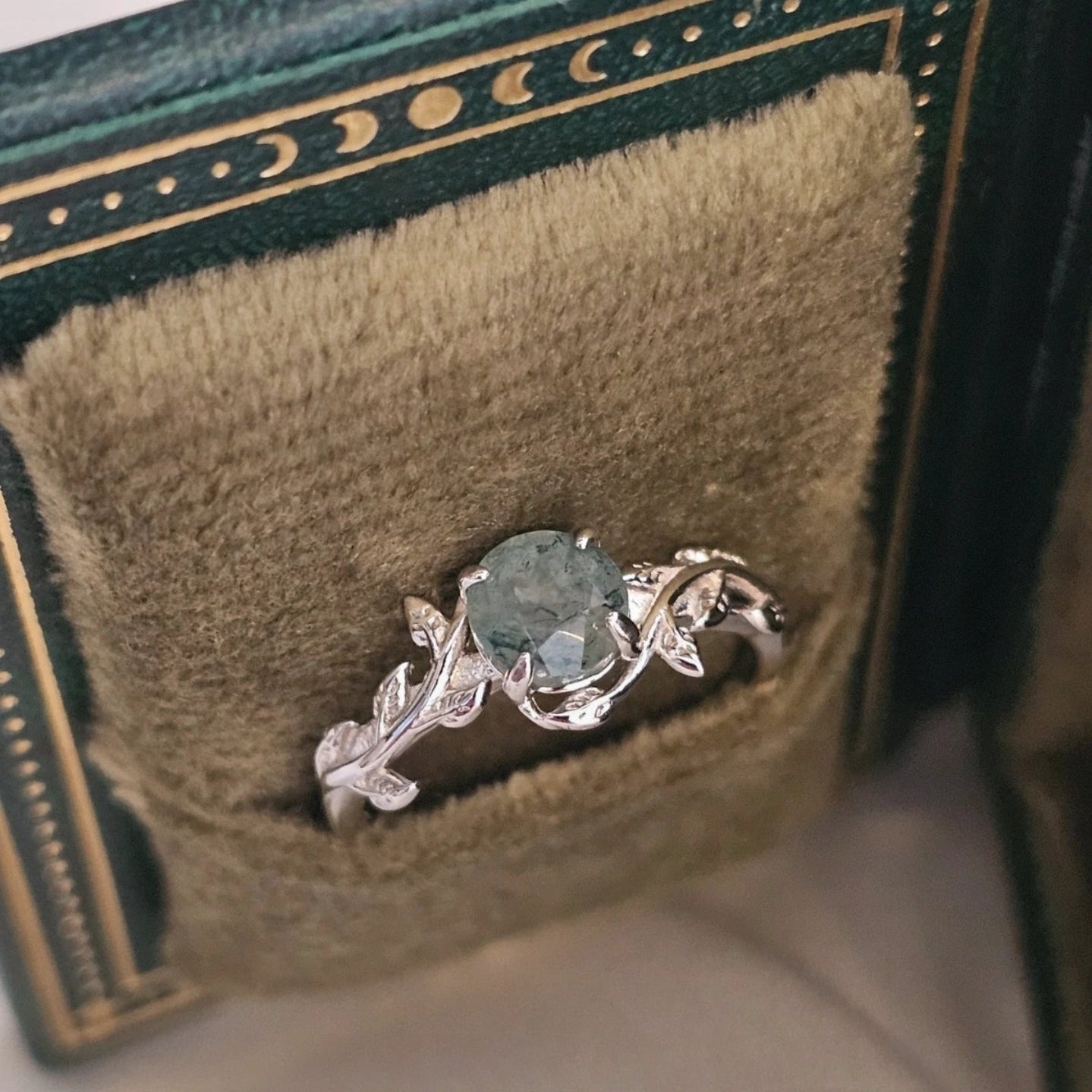 Silver ring with a green moss agate gemstone on a green velvet cushion